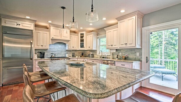 A modern kitchen with white cabinets, a large island with bar stools, stainless steel appliances, and pendant lighting.