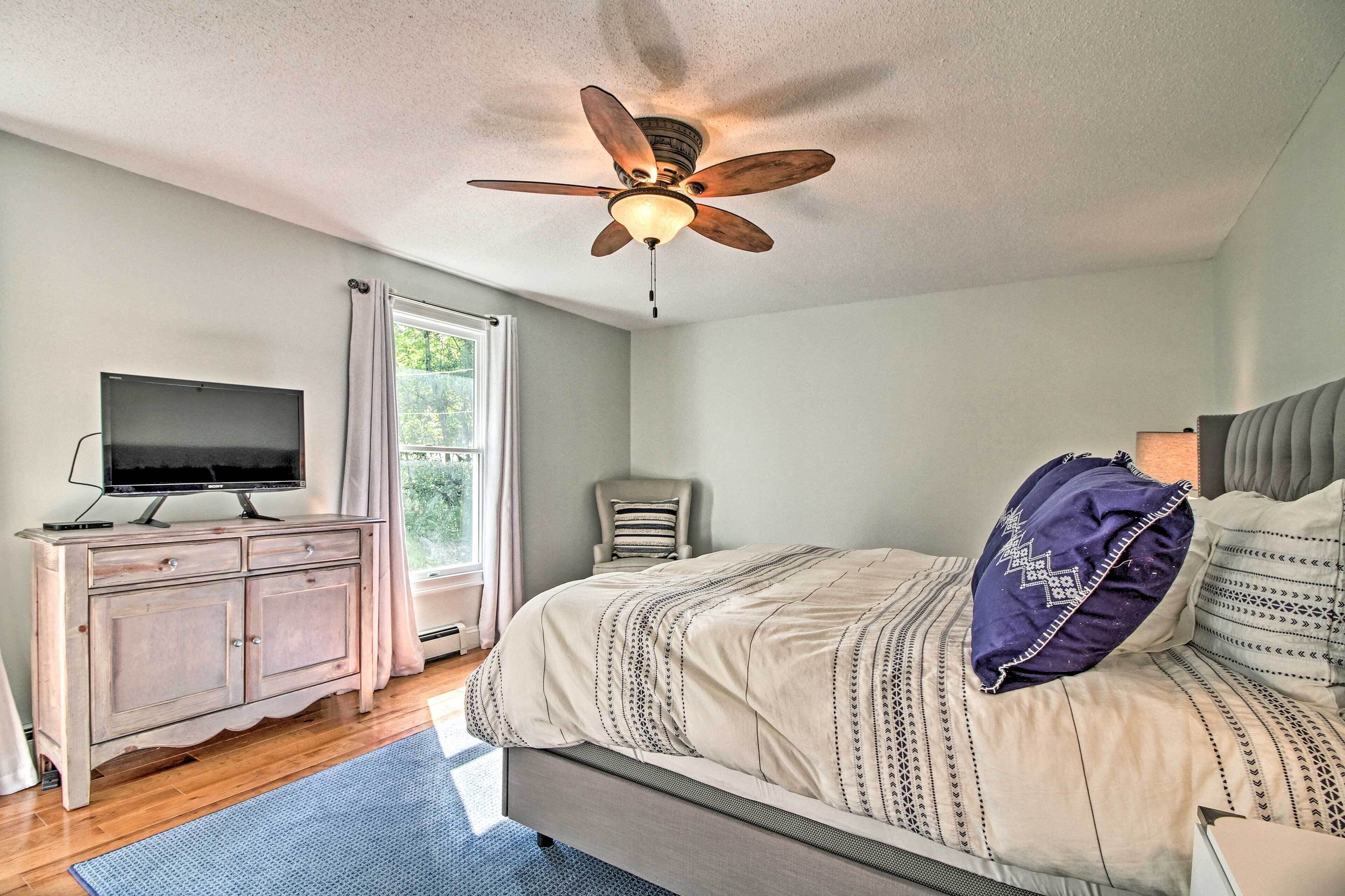 A bedroom with a bed, a television on a dresser, a ceiling fan, and a window with curtains.