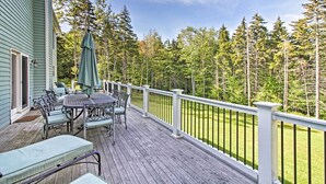 A wooden deck with outdoor furniture, a white railing, and a view of a forest.