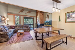 A spacious living room with a large sectional sofa, a wooden dining table, and a fireplace.
