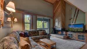 A cozy living room with a sectional sofa, a fireplace, a television, and ski equipment on the wall.