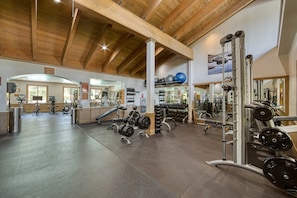 Un gimnasio con equipo de ejercicio variado, vigas de madera en el techo y un espejo grande.
