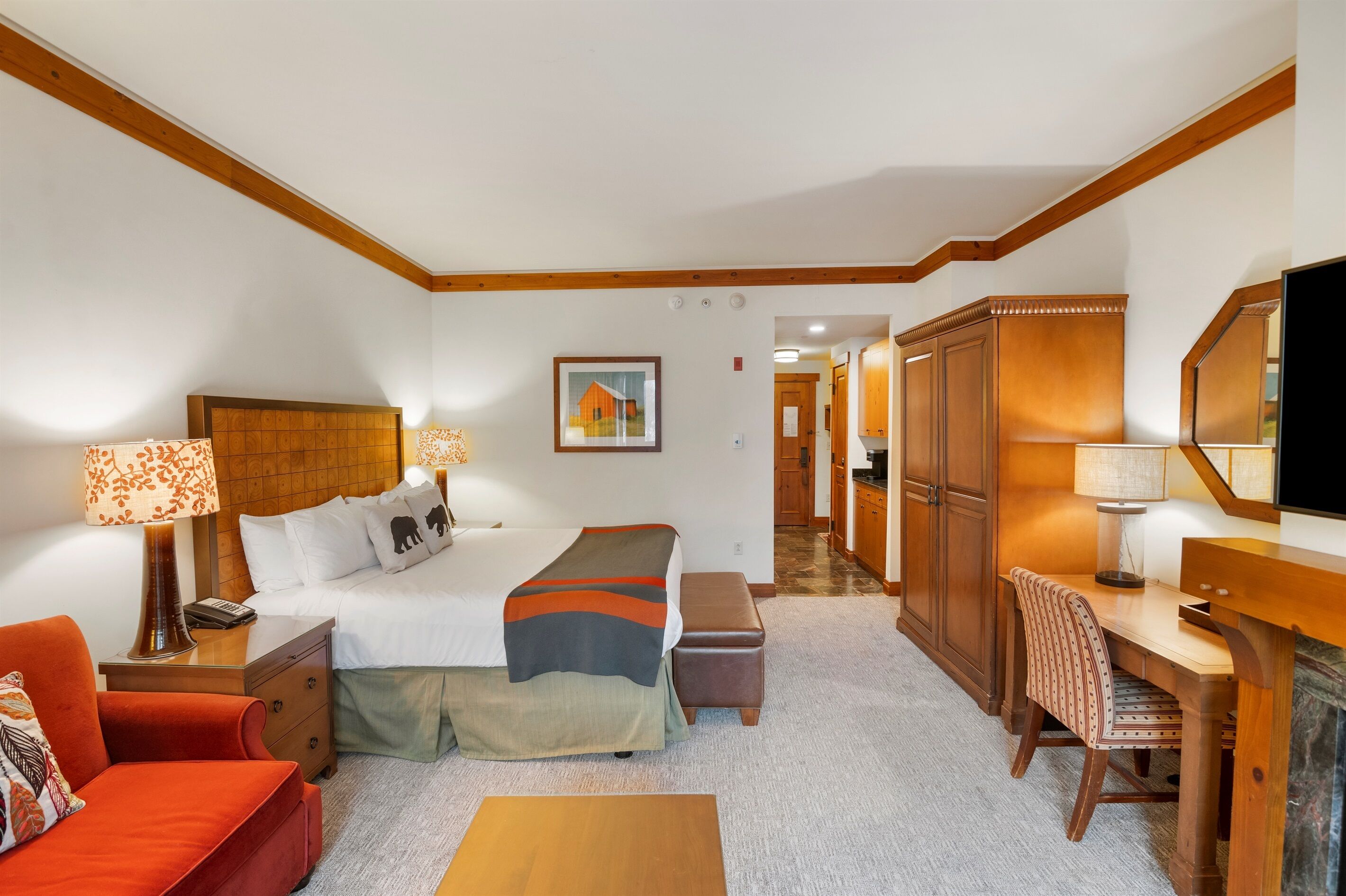 Ein Hotelzimmer mit Bett, Nachttisch, Lampe, Sessel, Schreibtisch und Fernseher.