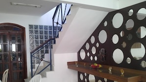 A staircase with a modern design, a dining area with a table and chairs, and a decorative wall with circular cutouts. - Garapuá Praia Hotel (Cairu)