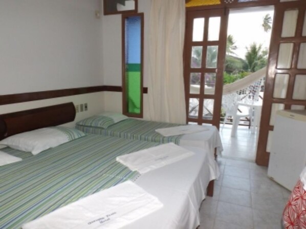 A hotel room with two beds, a small desk, and a balcony with a view of palm trees.