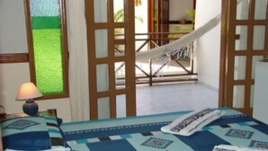 A bedroom with a bed, a nightstand, a lamp, and a view of a hammock outside. - Garapuá Praia Hotel (Cairu)