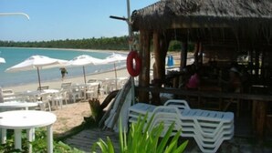A beachside restaurant with outdoor seating, a thatched roof, and a view of the ocean. - Garapuá Praia Hotel (Cairu)