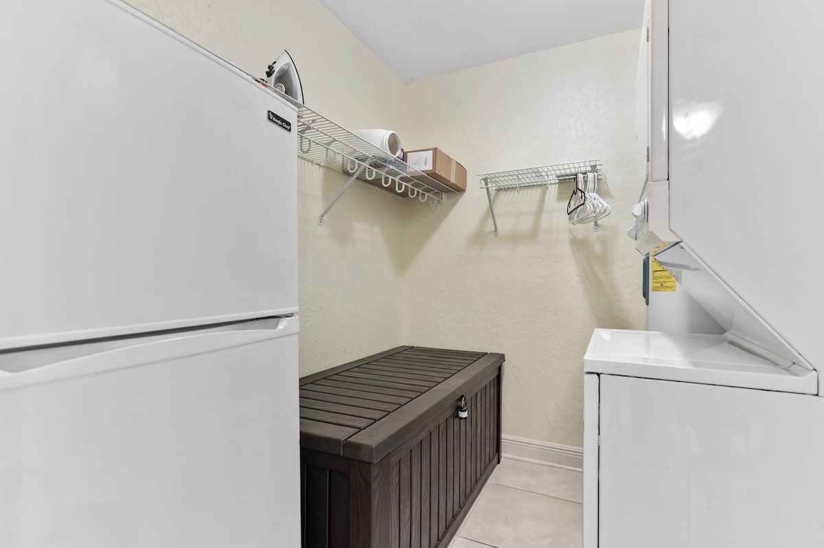 Une buanderie équipée d’un lave-linge blanc, d’un étendoir et d’un meuble de rangement.