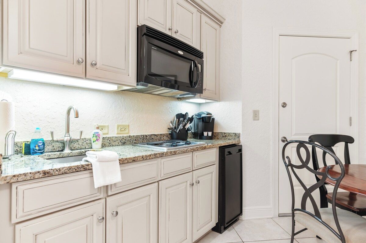 A kitchen with a dishwasher, a microwave, and a sink with a faucet. There is a chair and a table in the dining area.