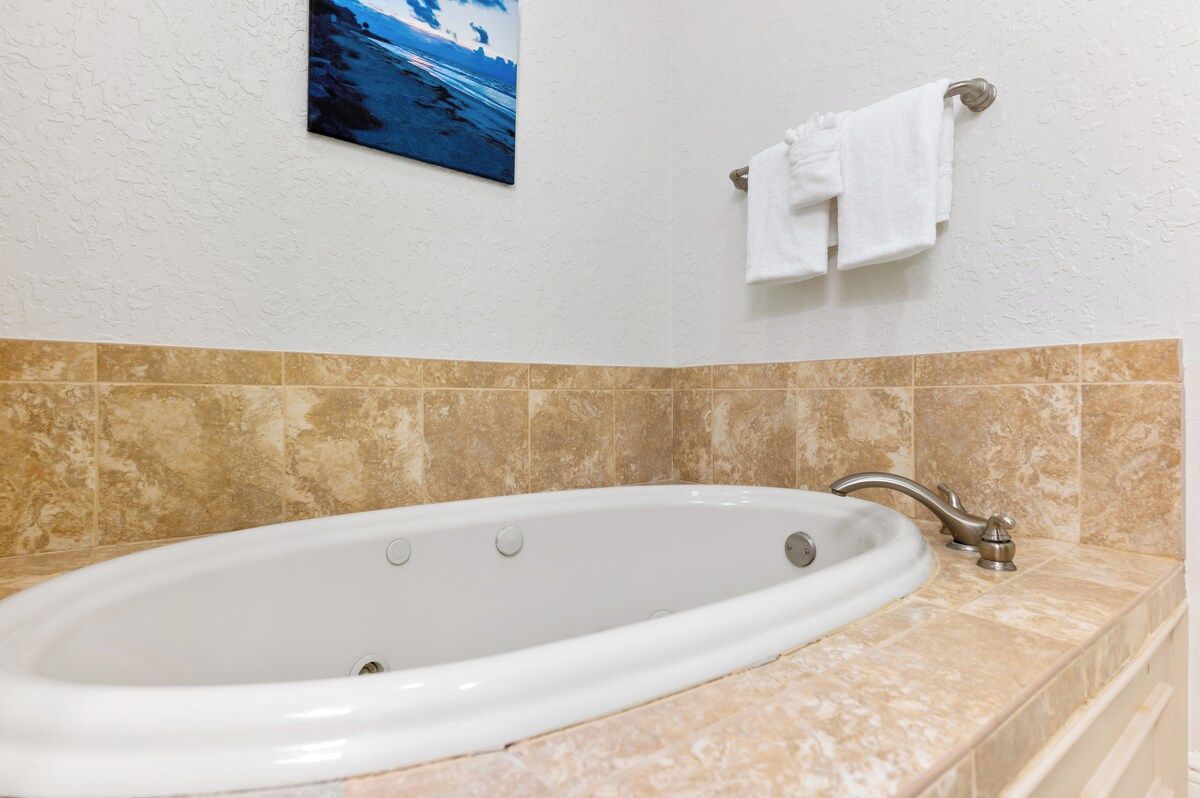 A bathroom with a bathtub, a towel rack with a white towel, and a painting on the wall.