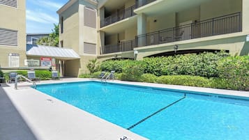 Una piscina con un cartello che indica divieto di tuffi, sedie a sdraio e un edificio con balconi.