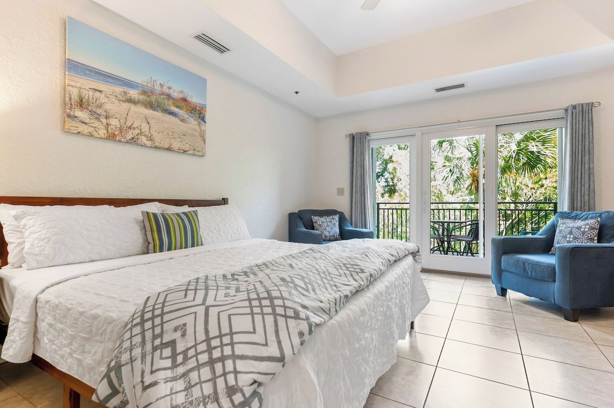 A bedroom with a bed, a chair, and a balcony with a view.