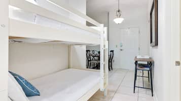 A bunk bed room with a desk and chairs, a door, and a hanging light fixture.
