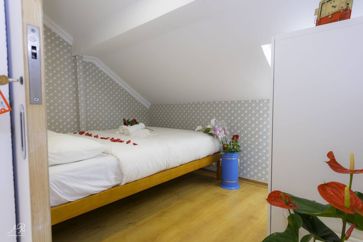 Una cama individual con sábanas blancas, cabecera de madera y un florero azul con flores.