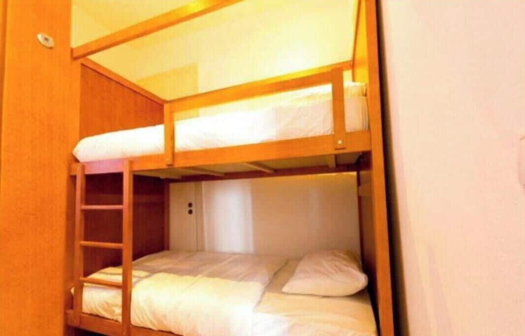 Een stapelbed met een ladder, een wit kussen en een houten hoofdbord.