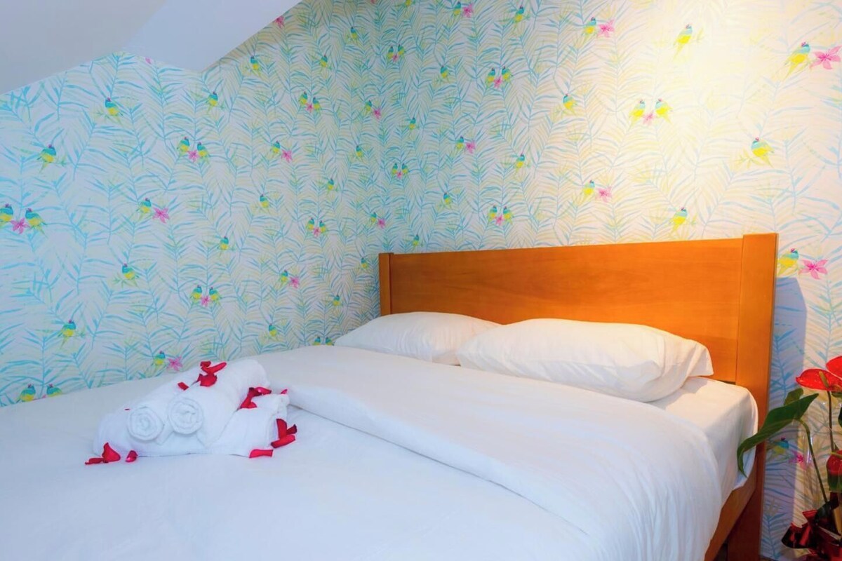 A neatly made bed with white linens and red decorative pillows, set against a floral wallpaper.