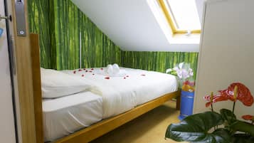Una cama individual con sábanas blancas, un muro con estampado de bambú, un tragaluz y un cubo de basura azul con flores.
