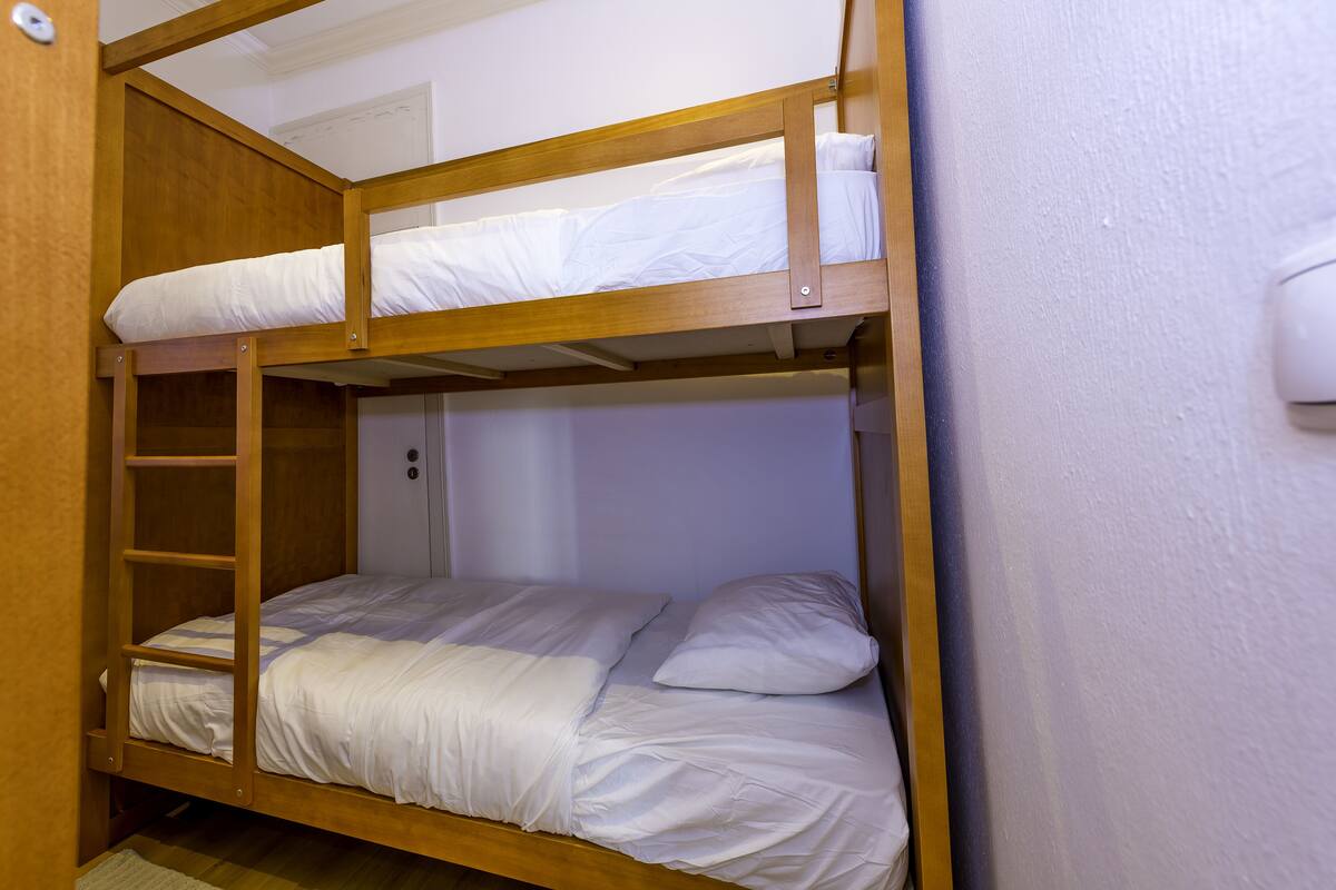 Una cama nido con escalera, ropa de cama blanca y estructura de madera.