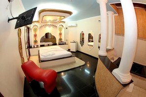Habitació d'hotel amb llit, una cadira vermella, televisió de pantalla plana penjada a la paret i bany amb banyera i vàter.