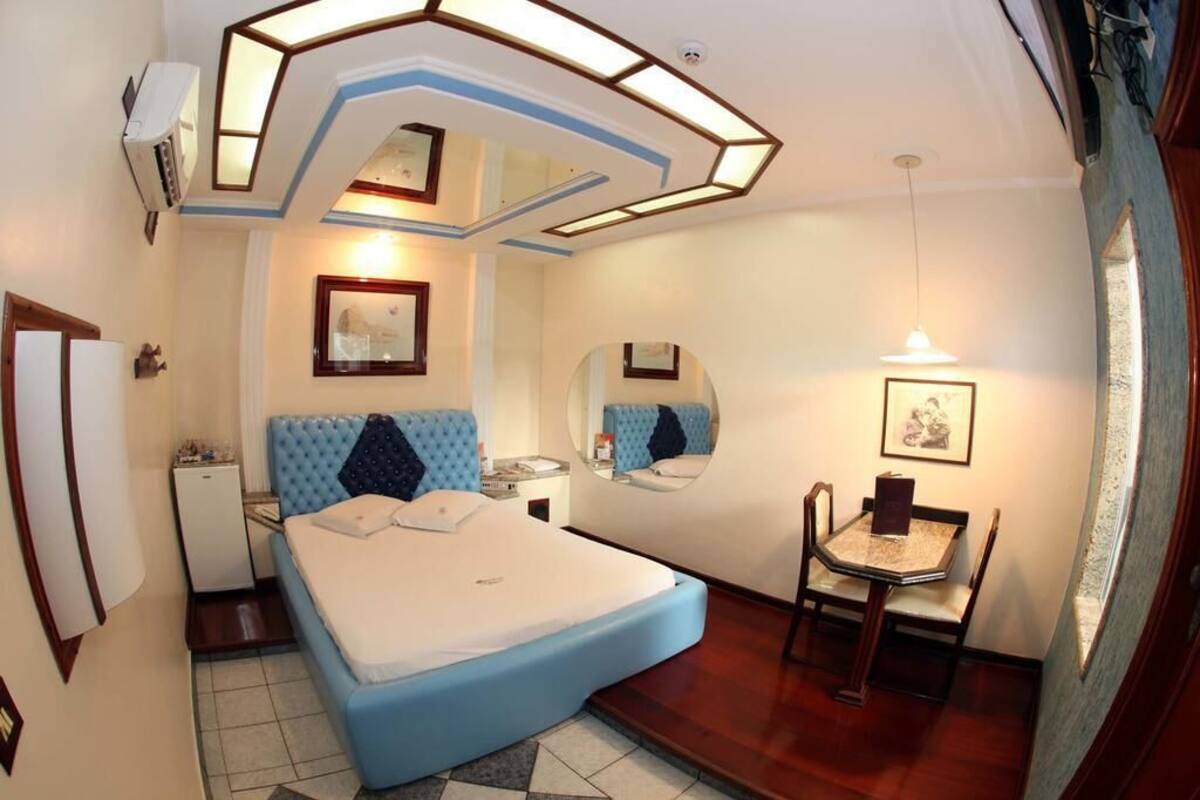 Un dormitorio con cama, escritorio, silla, espejo y una mesita.