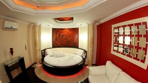 A circular bed with a white headboard, a red accent wall, and a large rose painting above it. - Hotel & Motel Le Baron (Porto Ferreira)