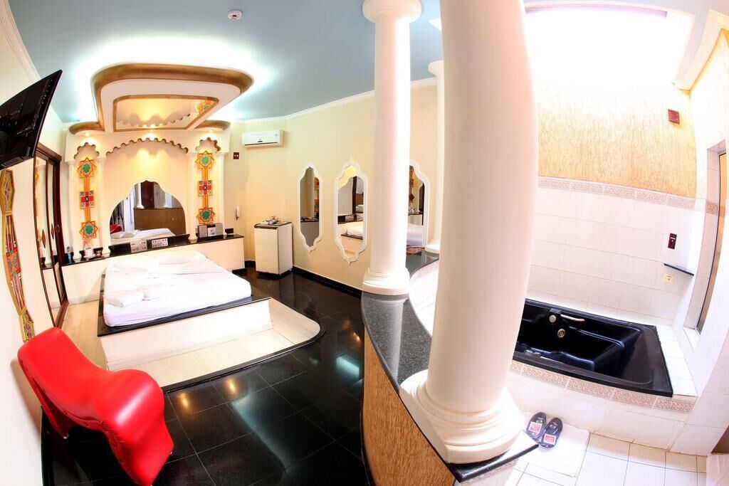 A modern spa room with a massage table, a red chair, a large mirror, and a bathtub.