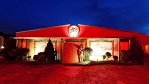 A building with a red facade and a prominent circular logo at the entrance. - Hotel & Motel Le Baron (Porto Ferreira)