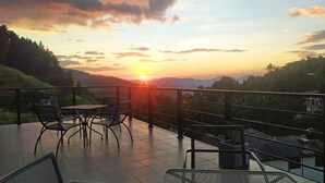 Une terrasse avec des chaises et une table, offrant une vue panoramique sur un paysage magnifique, notamment au coucher du soleil.