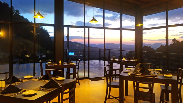 Un restaurant doté de nombreuses tables et chaises, de grandes fenêtres offrant une vue sur les montagnes et de luminaires suspendus.