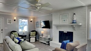 A living room with a fireplace, a ceiling fan, and a TV mounted on the wall.