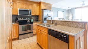 A modern kitchen with wooden cabinets, stainless steel appliances, granite countertops, and a dishwasher. - Tybee Beach Club 125 | Easy Walk to Beach + Pool! (Tybee Island)