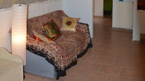 A cozy room with a stone wall, a patterned sofa, a hanging light fixture, and a framed picture. - Agriturismo Le Casette (Guardistallo)