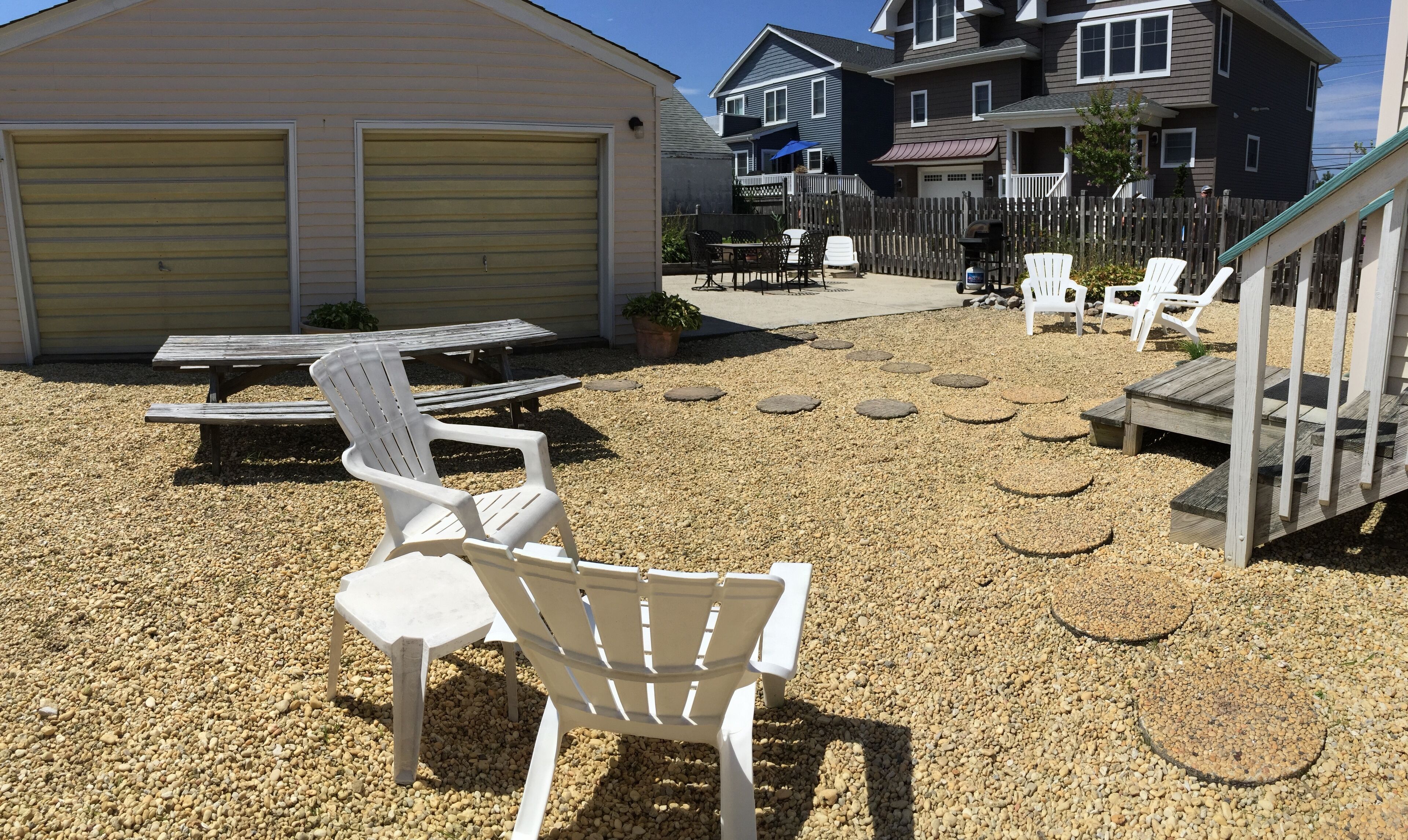 A backyard with a patio area, including a table and chairs, a barbecue grill, and a wooden deck.