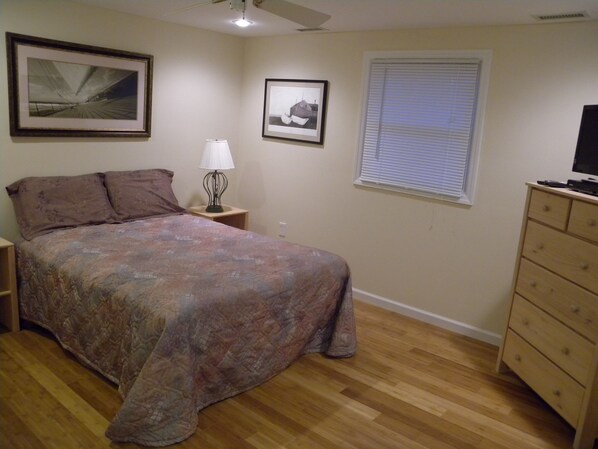 Une chambre à coucher comprenant un lit, une table de chevet, une lampe, une commode, un ventilateur de plafond et deux tableaux encadrés accrochés au mur.