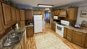 Una cocina con armarios de madera, un lavamanos de acero inoxidable, un refrigerador, una estufa y un microondas.