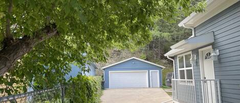 A residential garage with a white garage door, a covered porch with white railings, and a tree with green leaves in the foreground.