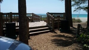 Eine Holzterrasse führt zum Strand, umgeben von Bäumen und mit freiem Blick auf das Meer.