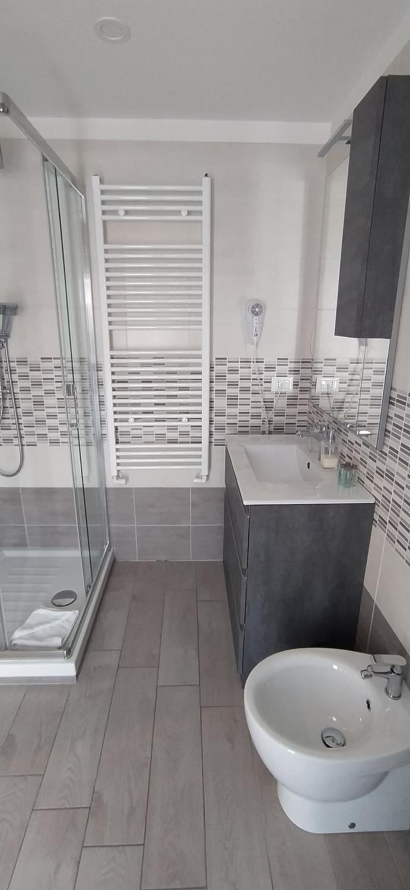 Un baño moderno con cabina de ducha de vidrio, un lavabo blanco y un mueble de tocador de tonos oscuros.