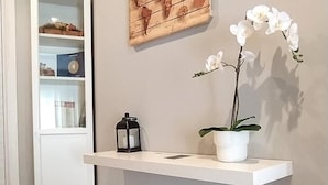 Un couloir avec une étagère blanche sur laquelle sont posés un pot d’orchidée et une lanterne, une carte du monde en guise d’œuvre d’art au mur, et une boîte blanche avec du texte posée sur le sol.