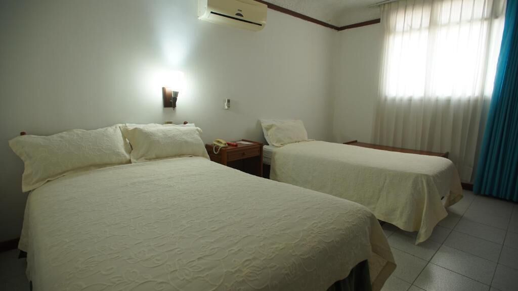 Habitació d'hotel amb dos llits, una tauleta de nit amb una làmpada, un telèfon i una finestra amb cortines.
