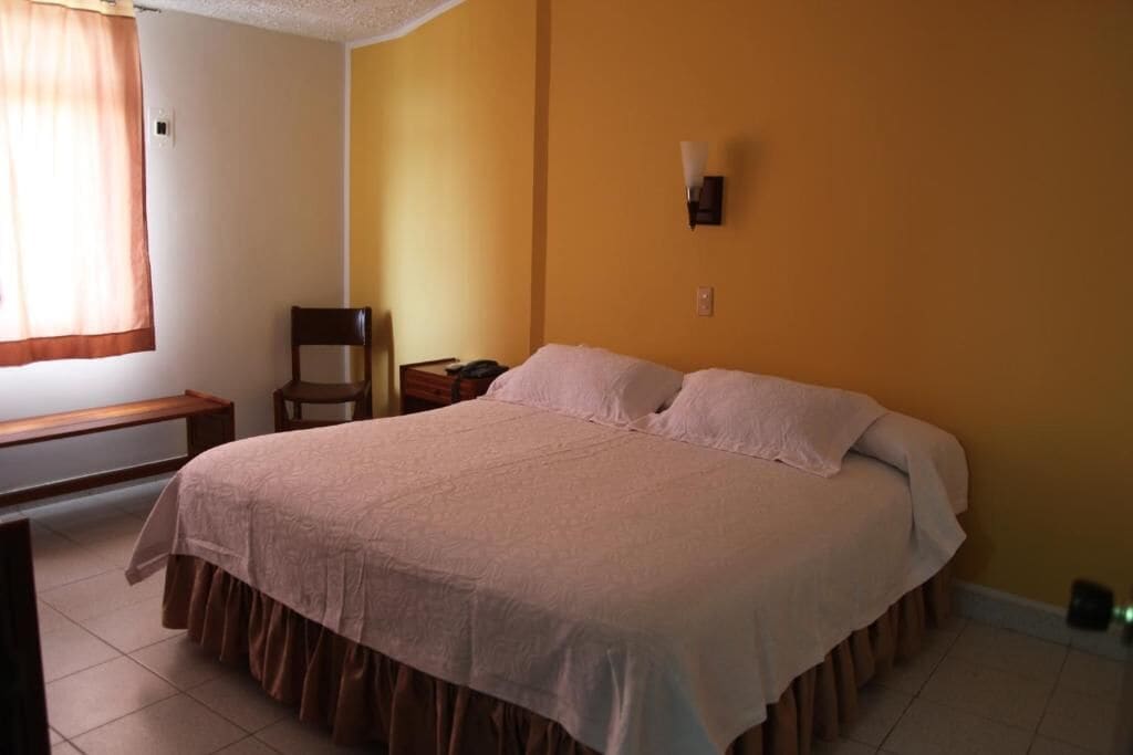 A bedroom with a bed, a chair, a nightstand, and a window with curtains.