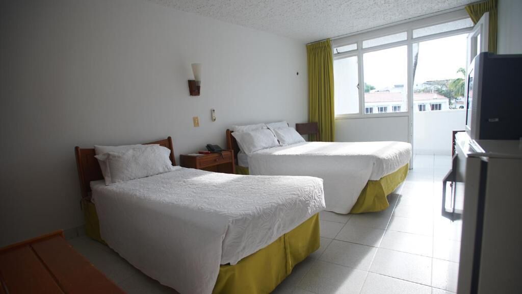 Una habitación de hotel con dos camas, televisión y ventana con cortinas.