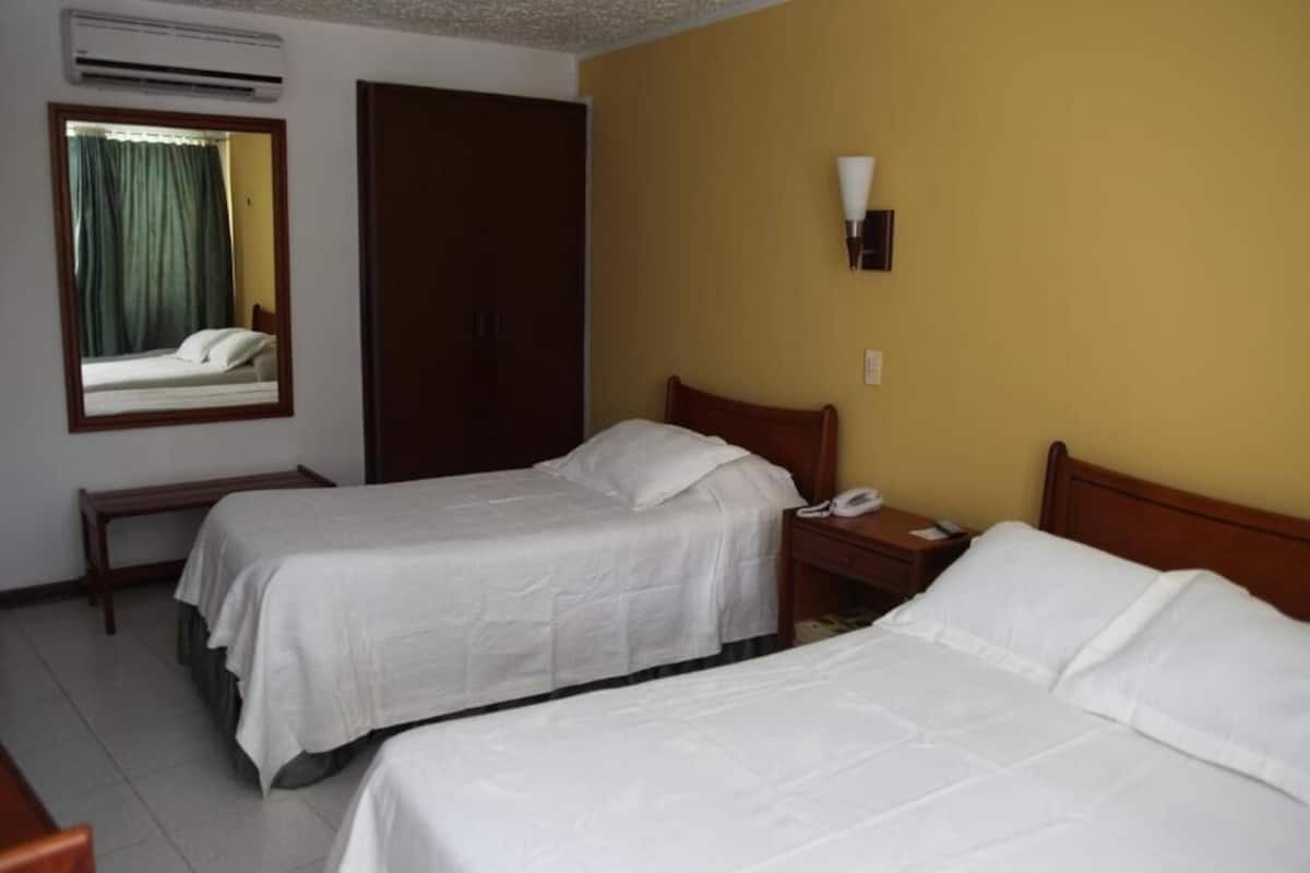 Une chambre d’hôtel avec deux lits simples, une table de chevet avec un téléphone, un miroir et un appareil de climatisation.