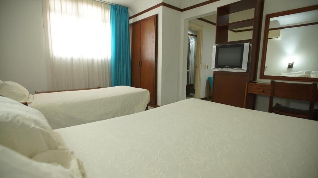 Habitación de hotel con dos camas, televisor, escritorio y armario.