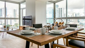 A dining area with a wooden table set for four, a TV, and a city view. - New Cozy Apartment Ocean View (Panama City)