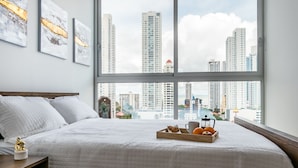 A hotel room with a large bed, a tray with snacks, and a city view through large windows. - New Cozy Apartment Ocean View (Panama City)