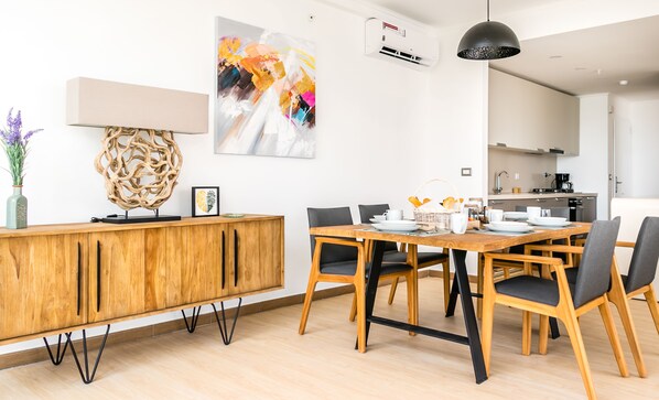 Un comedor moderno con una mesa y sillas de madera, un adorno en la pared y una cocina al fondo.
