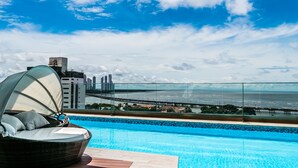 A rooftop pool with a view of the ocean and a bridge, a lounge chair, and a cityscape in the background. - New Elegant Ocean View (Panama City)
