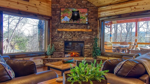 A cozy cabin interior with a stone fireplace, leather seating, and a television mounted on the wall.