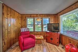 Relax in a warm room with a comfortable armchair, TV, and large windows with blinds.